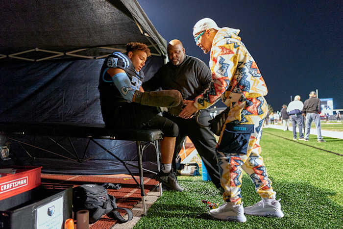Off the field and between tackles, Thomas gets encouragement—and adjustments on his “athletic leg”—from Devon and Josh.